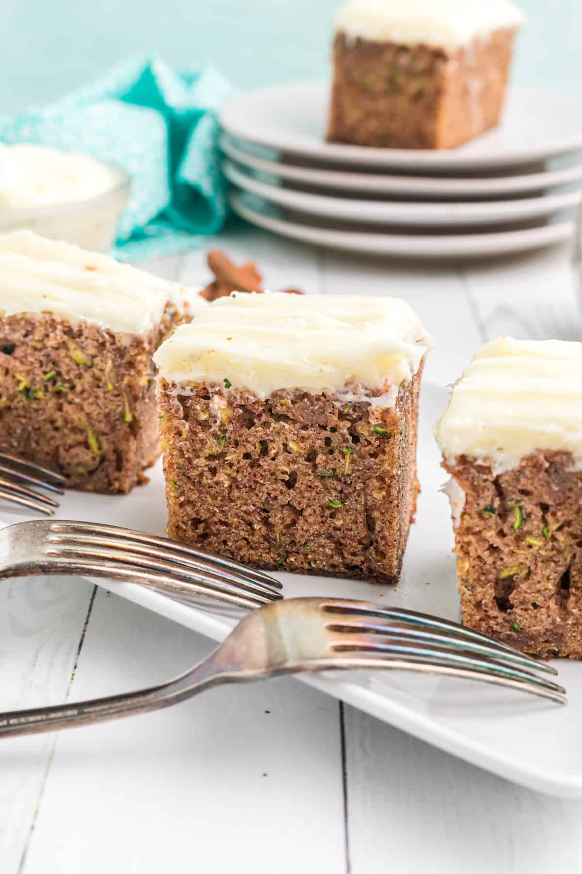 Several slices of zucchini cake are presented next to two forks on a white plate.