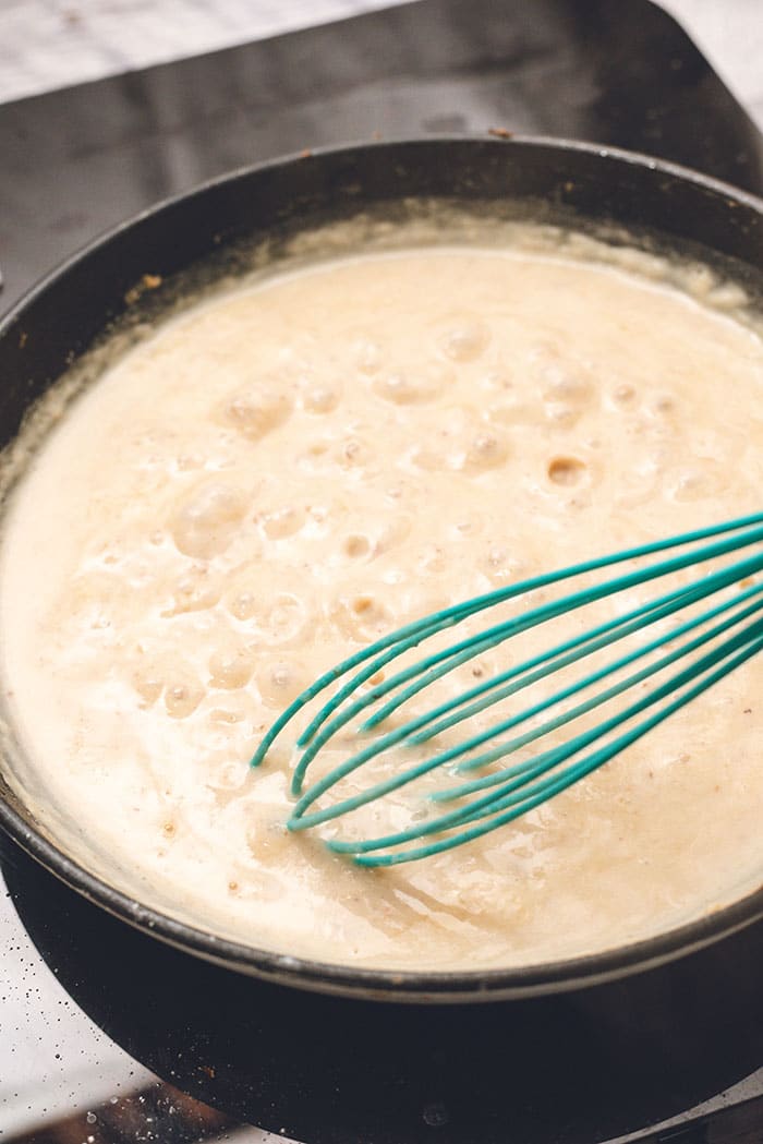 Cream sauce for baked gnocchi in a skillet with a blue whisk.