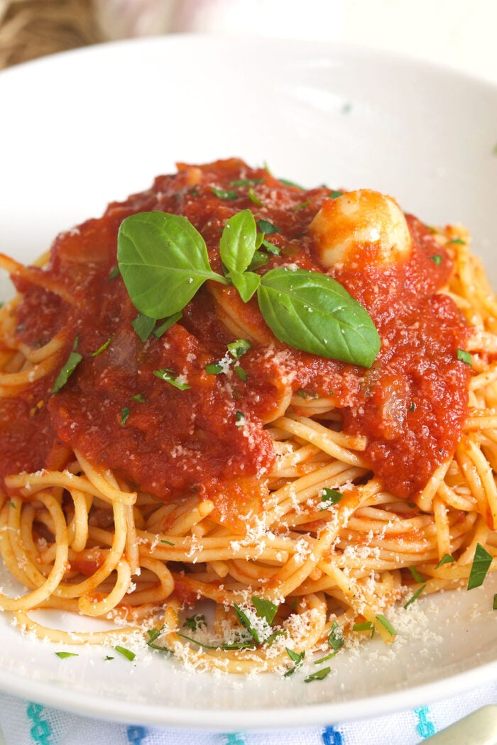 A serving of spaghetti is topped with marinara sauce and fresh herbs.