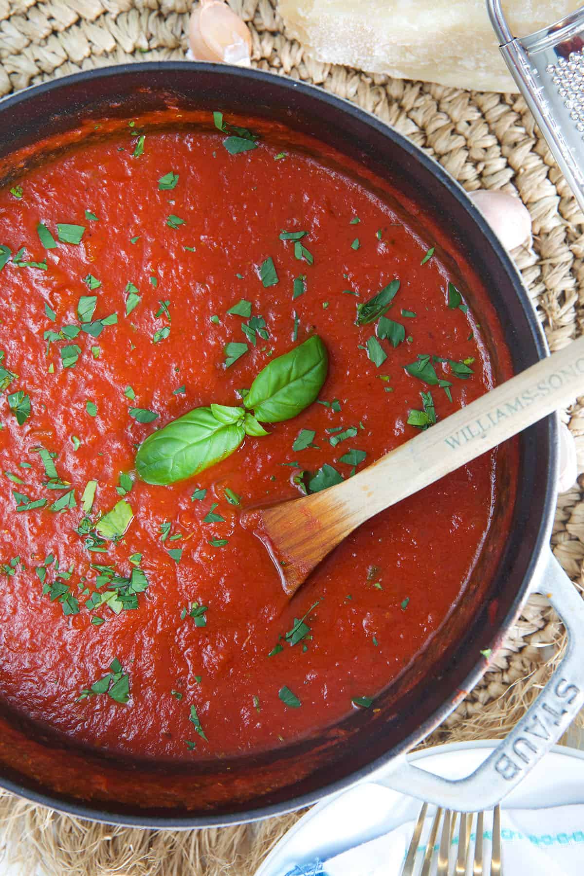 A large pot filled with red marinara sauce is being mixed with a wooden spoon.
