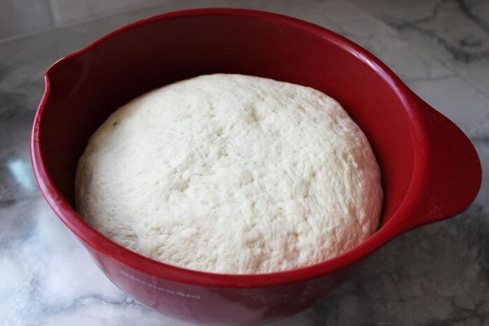 pizza dough rising in a red bowl