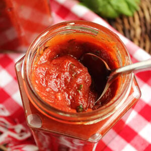 Red pizza sauce in a jar with a spoon in it.