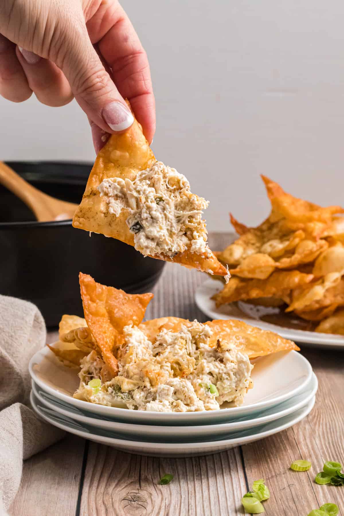 A chip that's topped with crab dip is being lifted by a hand from a white plate.