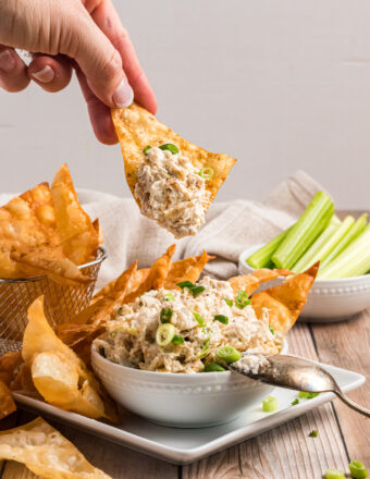 A chip is dipping into a small bowl of crab dip.