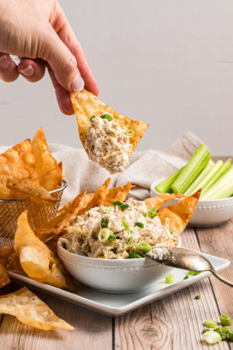 A chip is dipping into a small bowl of crab dip.