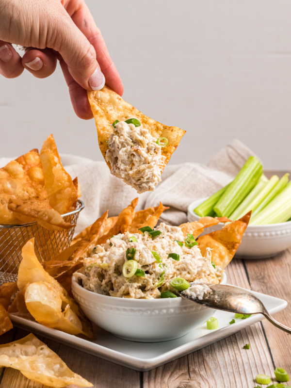 A chip is dipping into a small bowl of crab dip.