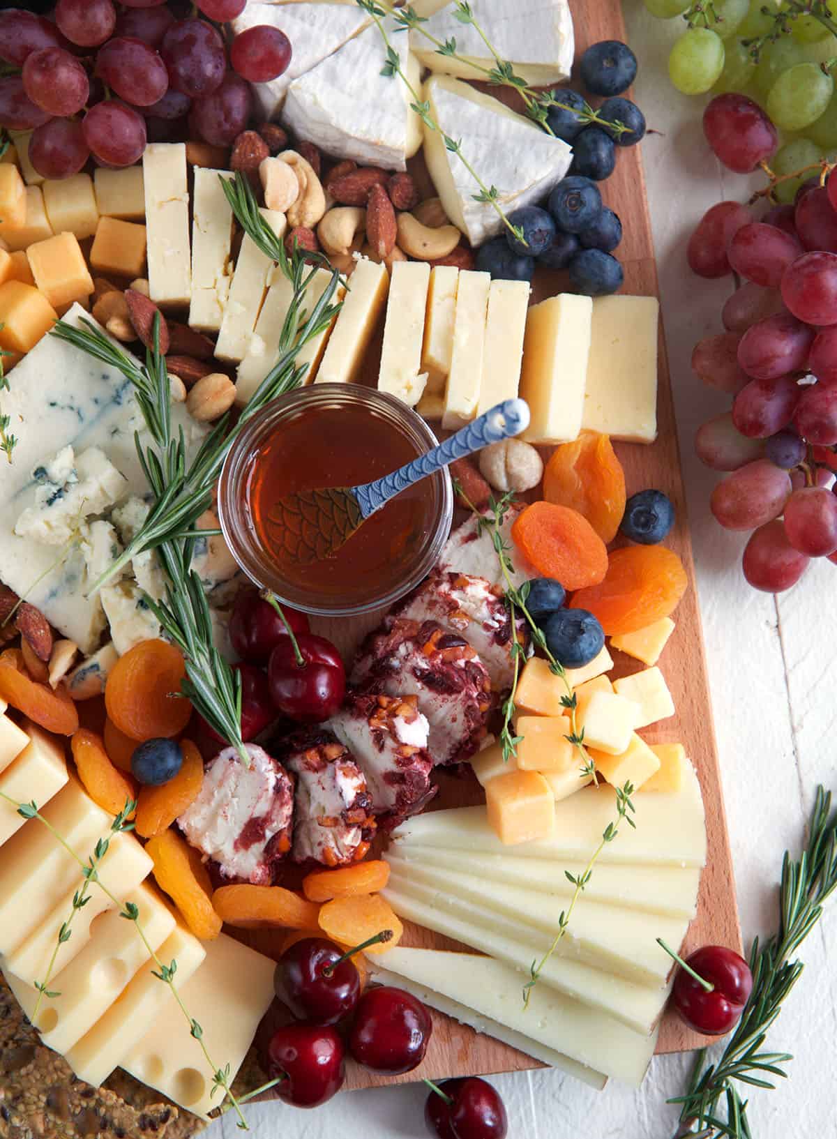 Overhead view of cheese board with fruit, sausage, honey, and more