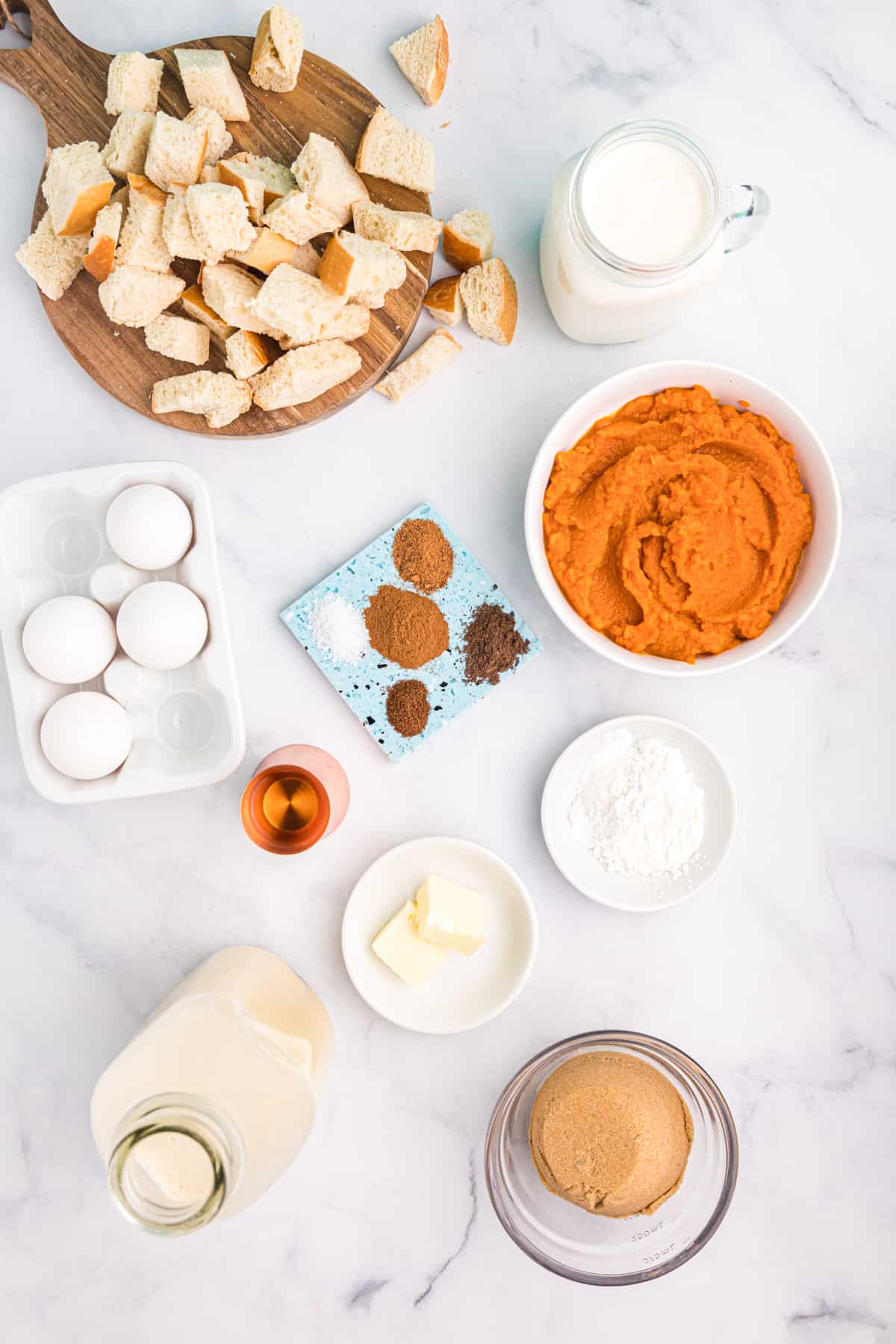 The ingredients for pumpkin bread pudding are placed on a white countertop.