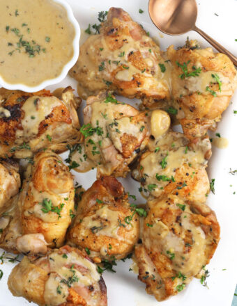 Braised chicken thighs on a white platter with a garlic white wine sauce in a bowl