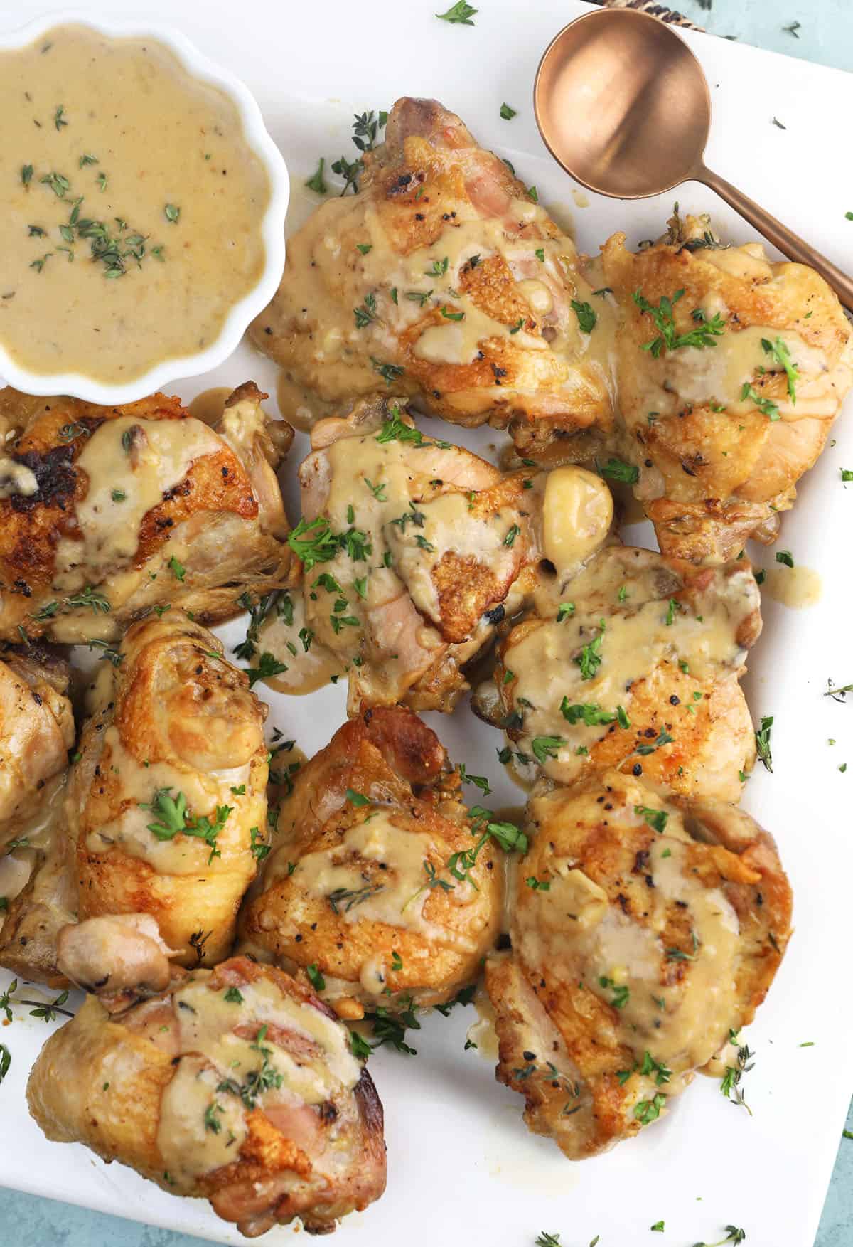 Braised chicken thighs on a white platter with a garlic white wine sauce in a bowl