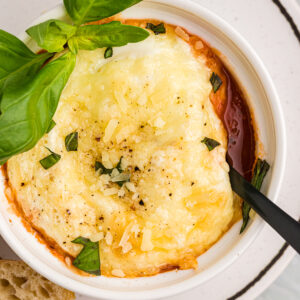 Italian Baked Eggs in a white ramekin with a sprig of basil and a fork in the dish.