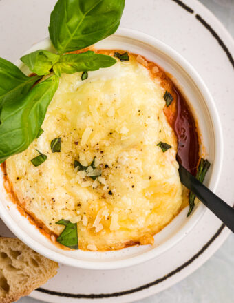 Italian Baked Eggs in a white ramekin with a sprig of basil and a fork in the dish.