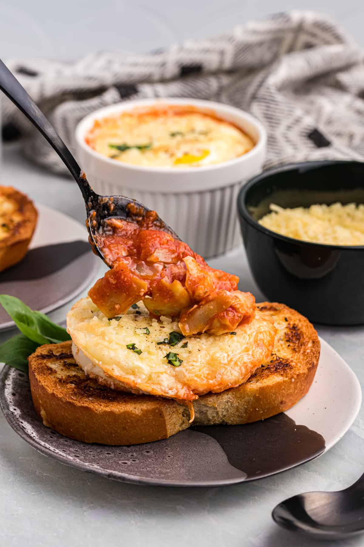 Baked eggs on a piece of toast being topped with tomato sauce.