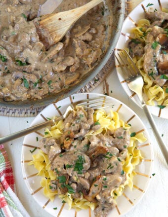 A plate of egg noodles is topped with beef stroganoff and placed next to a full skillet.