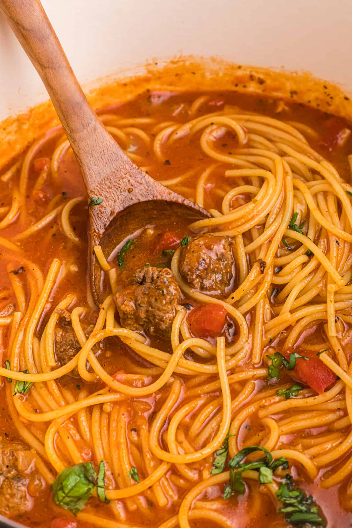 A wooden spoon is placed in a bowl of spaghetti and meatball stew.