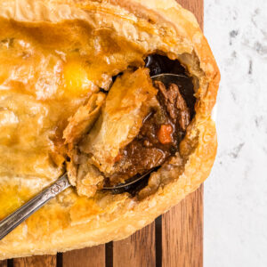 A metal spoon is scooping out a portion of beef pot pie.
