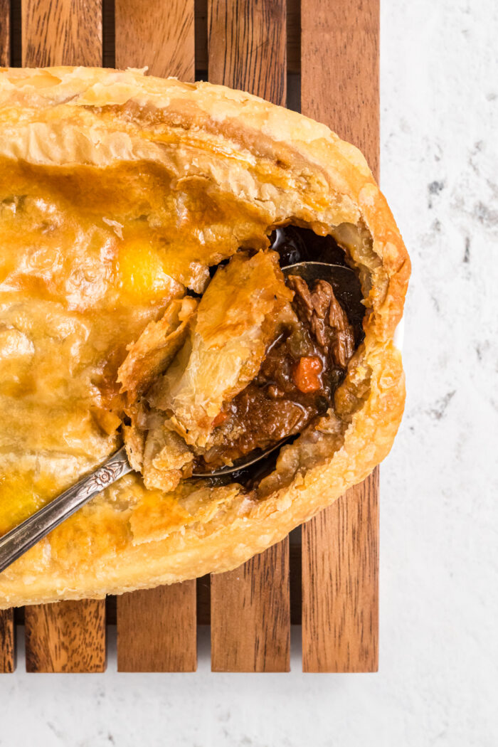 A metal spoon is scooping out a portion of beef pot pie.