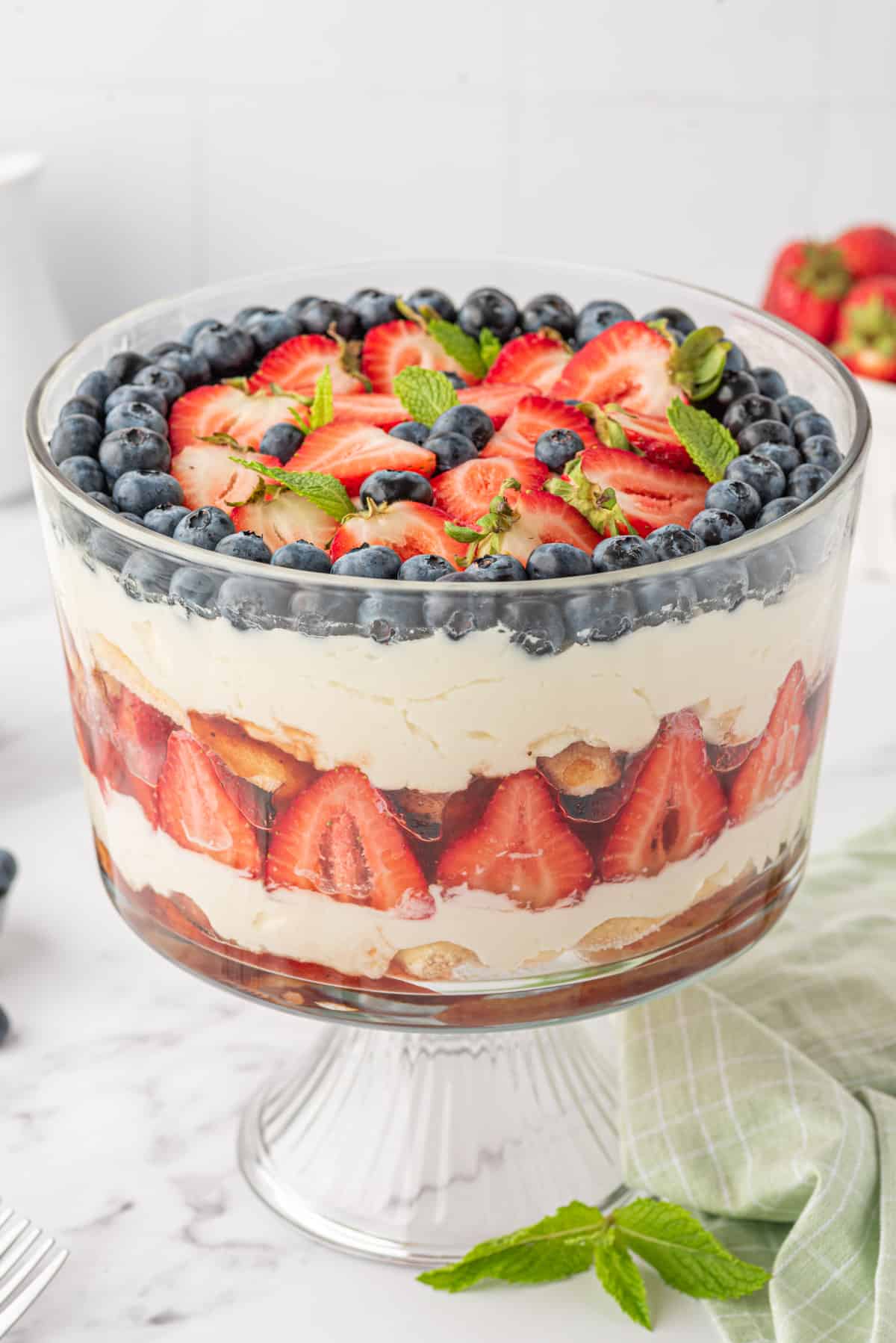 A layered strawberry and blueberry tiramusi is presented in a glass trifle dish.