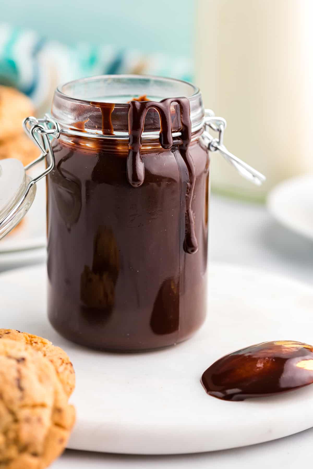 A jar of hot fudge sauce has a little drizzle on the outside of it.