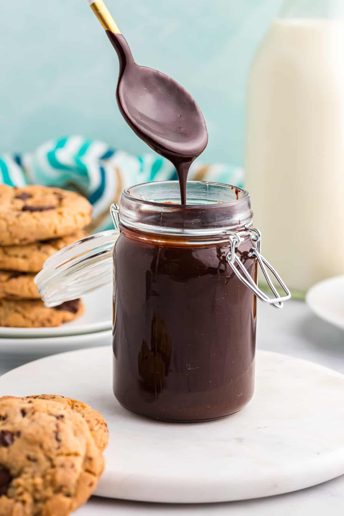 A spoon is drizzling hot fudge sauce into a full jar.