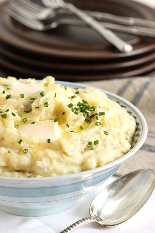 MASHED POTATOES IN A BLUE AND WHITE BOWL WITH CHIVES AND BUTTER ON TOP.