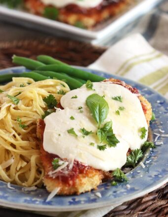 Chicken Parmesan on a blue plate with a side of spaghetti and garnished with tiny basil leaves.