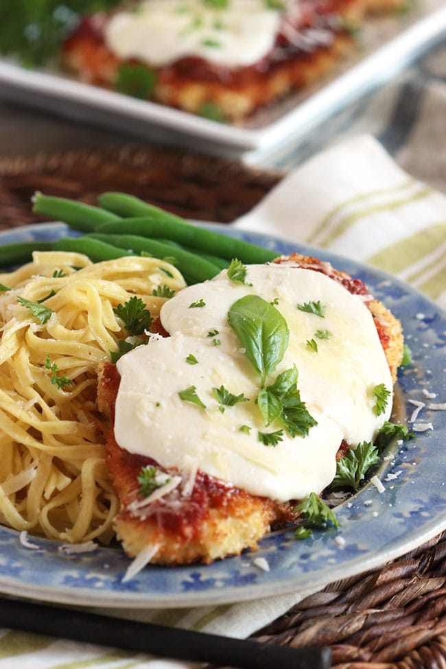 Healthier Oven Baked Chicken Parmesan on a blue plate with spaghetti and basil.