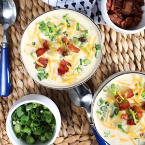 Overhead shot of two white bowls with Loaded Baked Potato Soup with a bowl of scallions and bacon on the side.