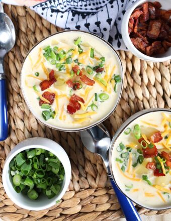 Overhead shot of two white bowls with Loaded Baked Potato Soup with a bowl of scallions and bacon on the side.