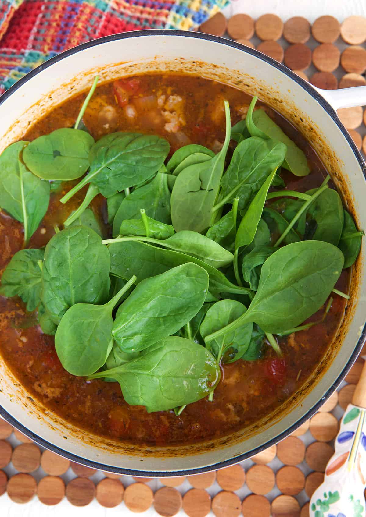 Overhead view of spinach added to pot of Italian sausage soup