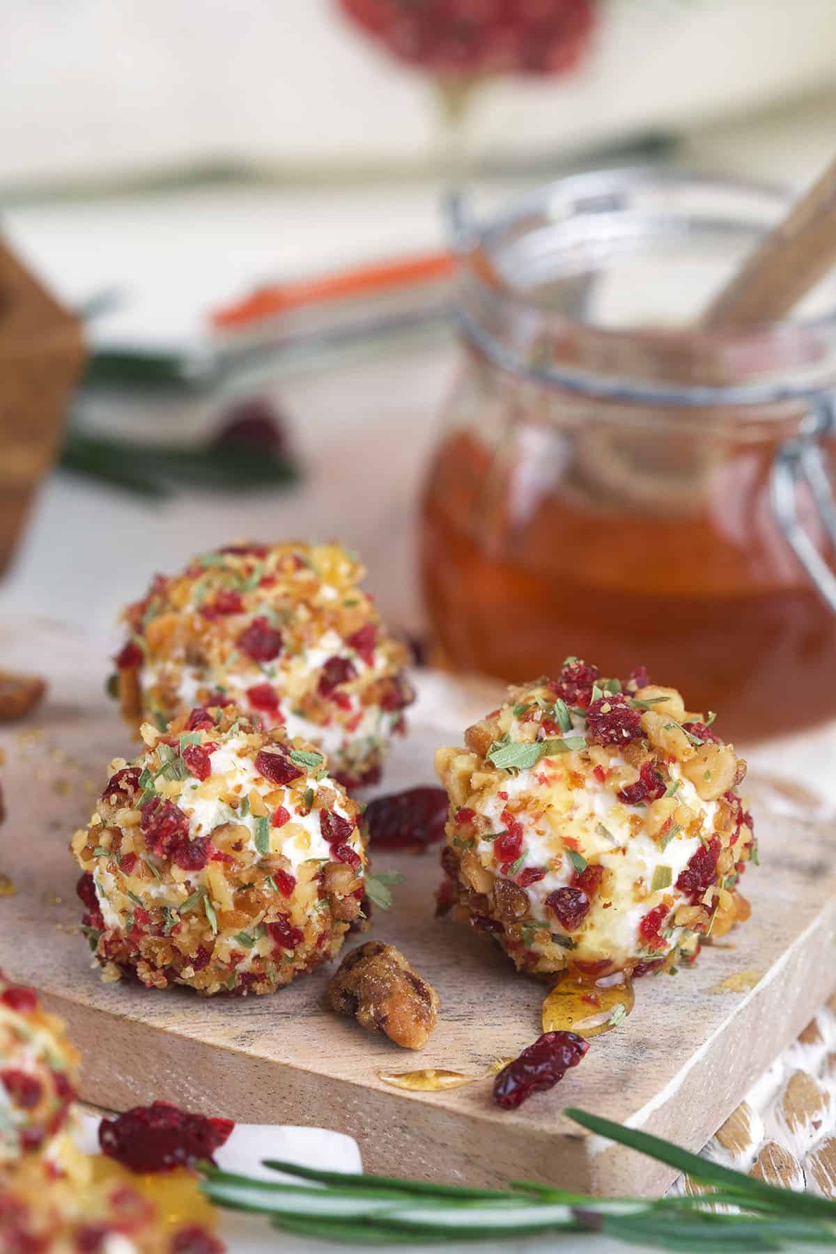 Goat cheese balls on serving board with honey in jar in background