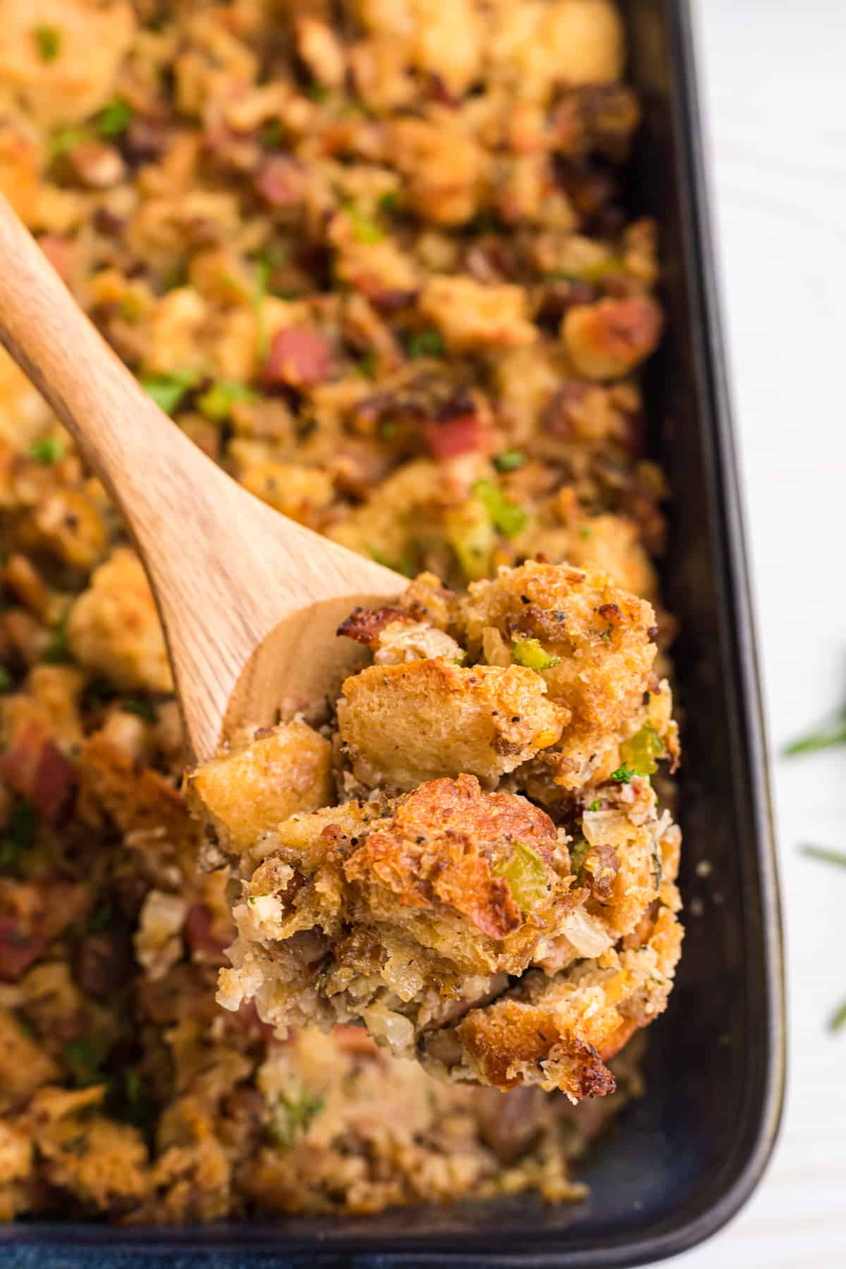 Some stuffing is being lifted from the baking dish with a wooden spoon.