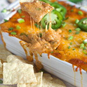 Chip being dipped into chili cheese dip in a white baking dish.