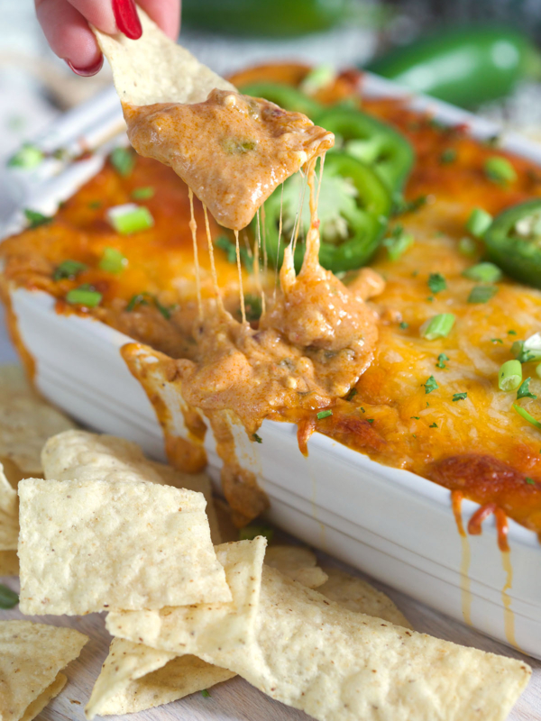 Chip being dipped into chili cheese dip in a white baking dish.