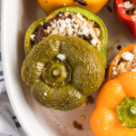 The tops of stuffed peppers are placed on top of them in a white baking dish.