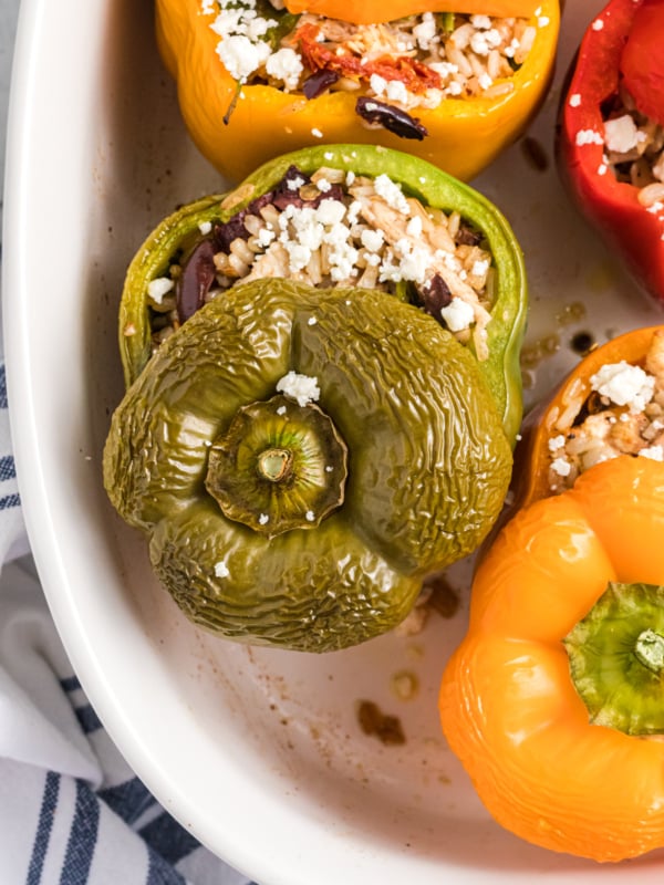 The tops of stuffed peppers are placed on top of them in a white baking dish.