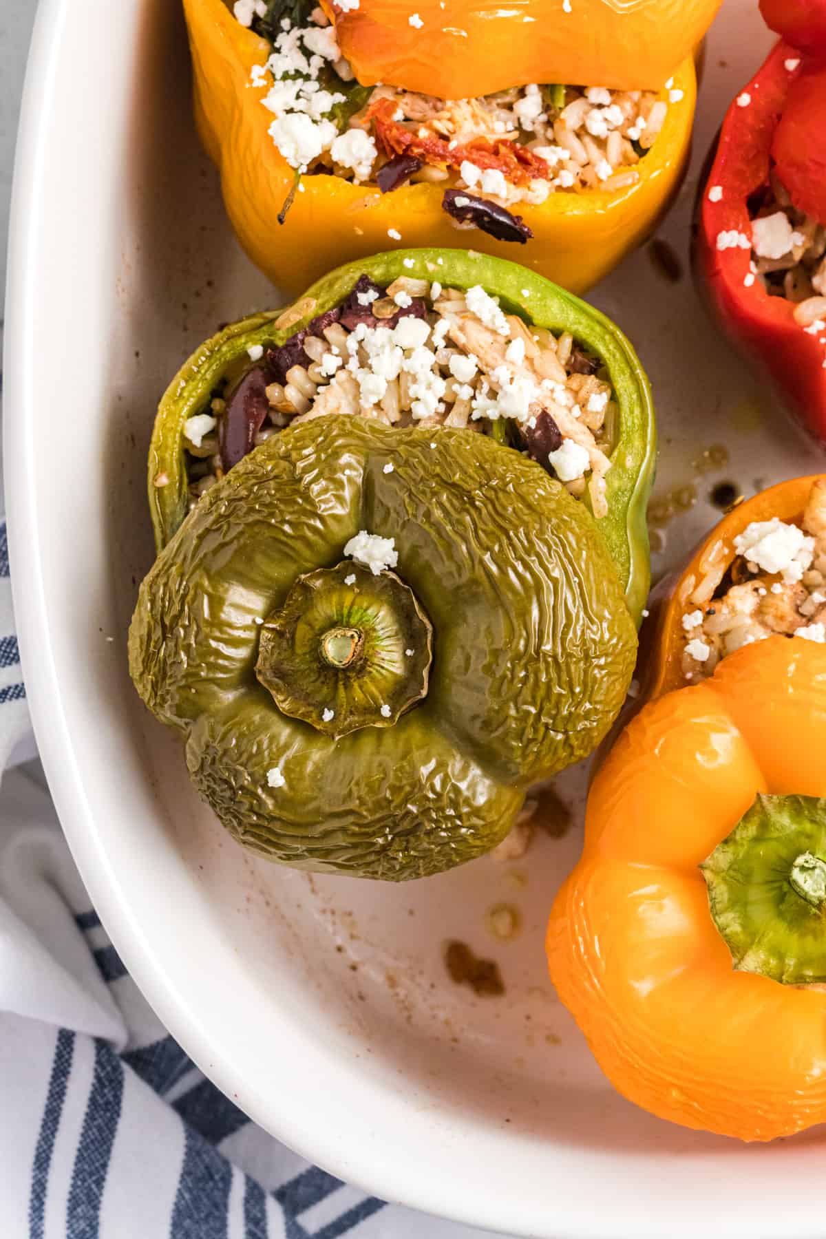 The tops of stuffed peppers are placed on top of them in a white baking dish.