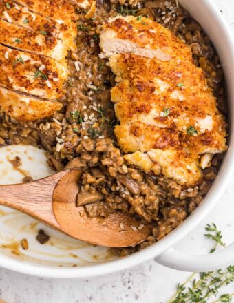 A wooden spoon is placed in a skillet filled with risotto and sliced chicken.