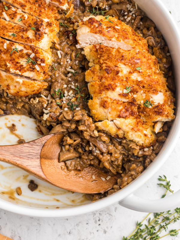 A wooden spoon is placed in a skillet filled with risotto and sliced chicken.