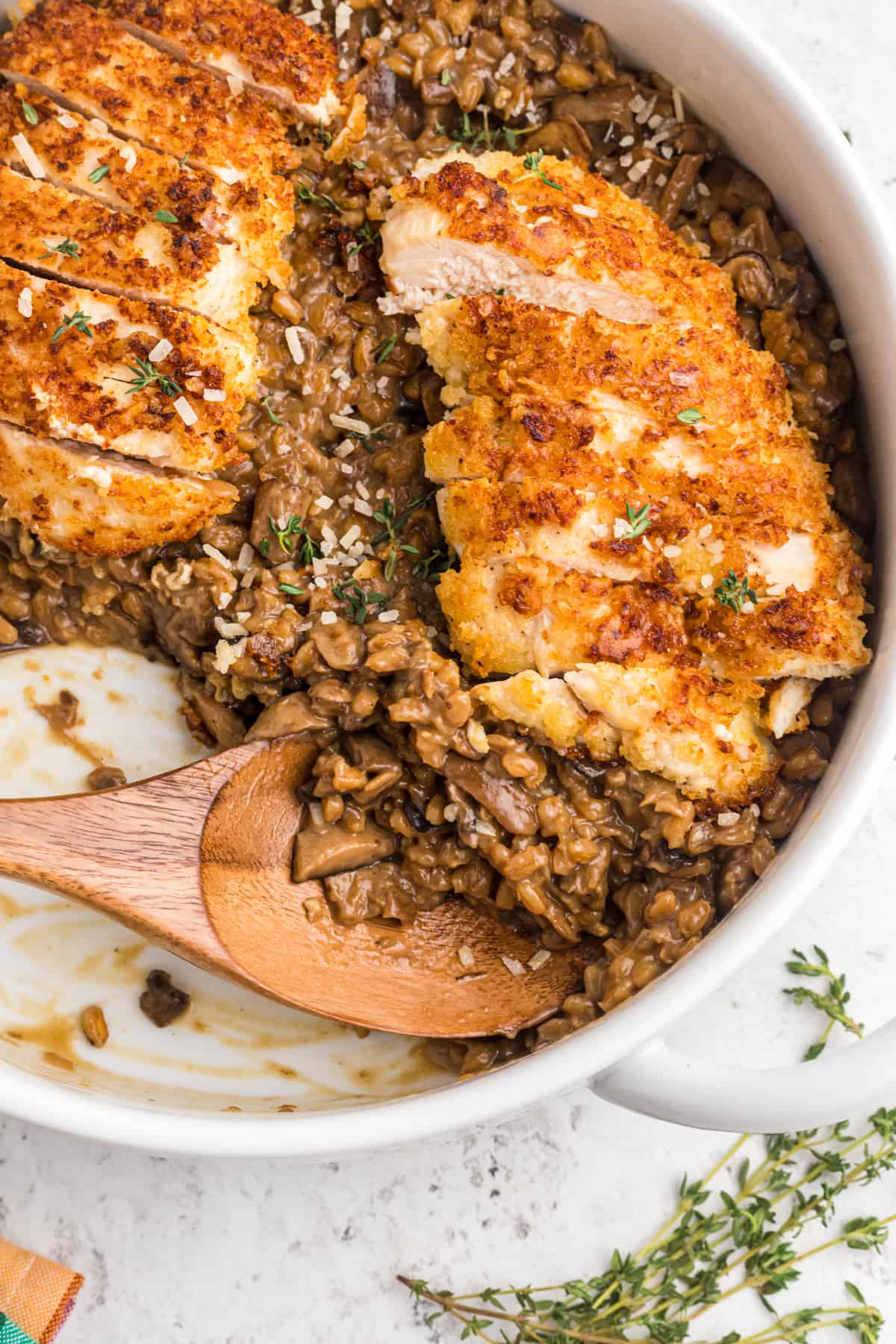 A wooden spoon is placed in a skillet filled with risotto and sliced chicken.