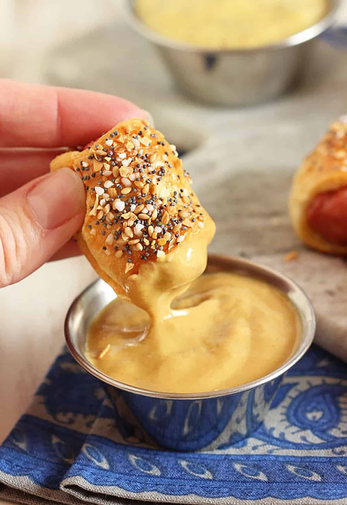 pigs in a blanket being dipped into mustard