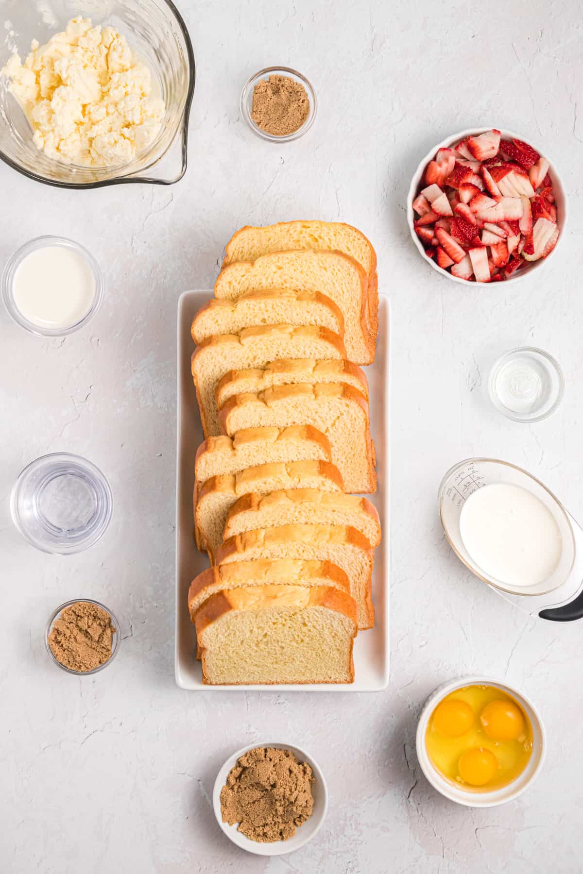 Sliced bread sits in the middle of a countertop and is surrounded by several different ingredients.