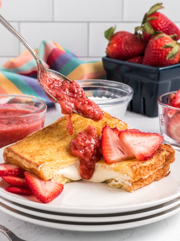 Starwberry compote is being drizzled atop a slice of stuffed french toast.