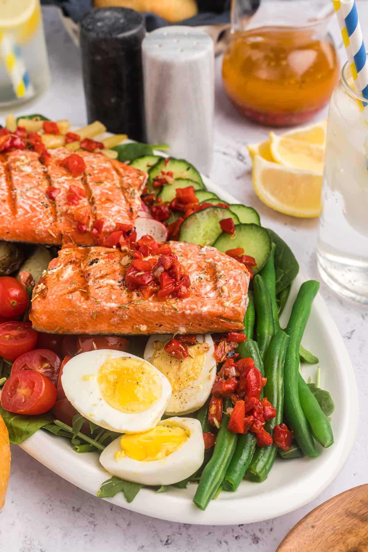 Side view of salmon Nicoise salad with hard boiled eggs, green beans and a roasted red pepper dressing.
