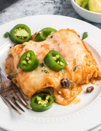 Several enchiladas are placed on a white plate and garnished with chopped jalapenos.