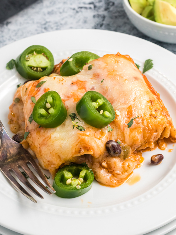 Several enchiladas are placed on a white plate and garnished with chopped jalapenos.