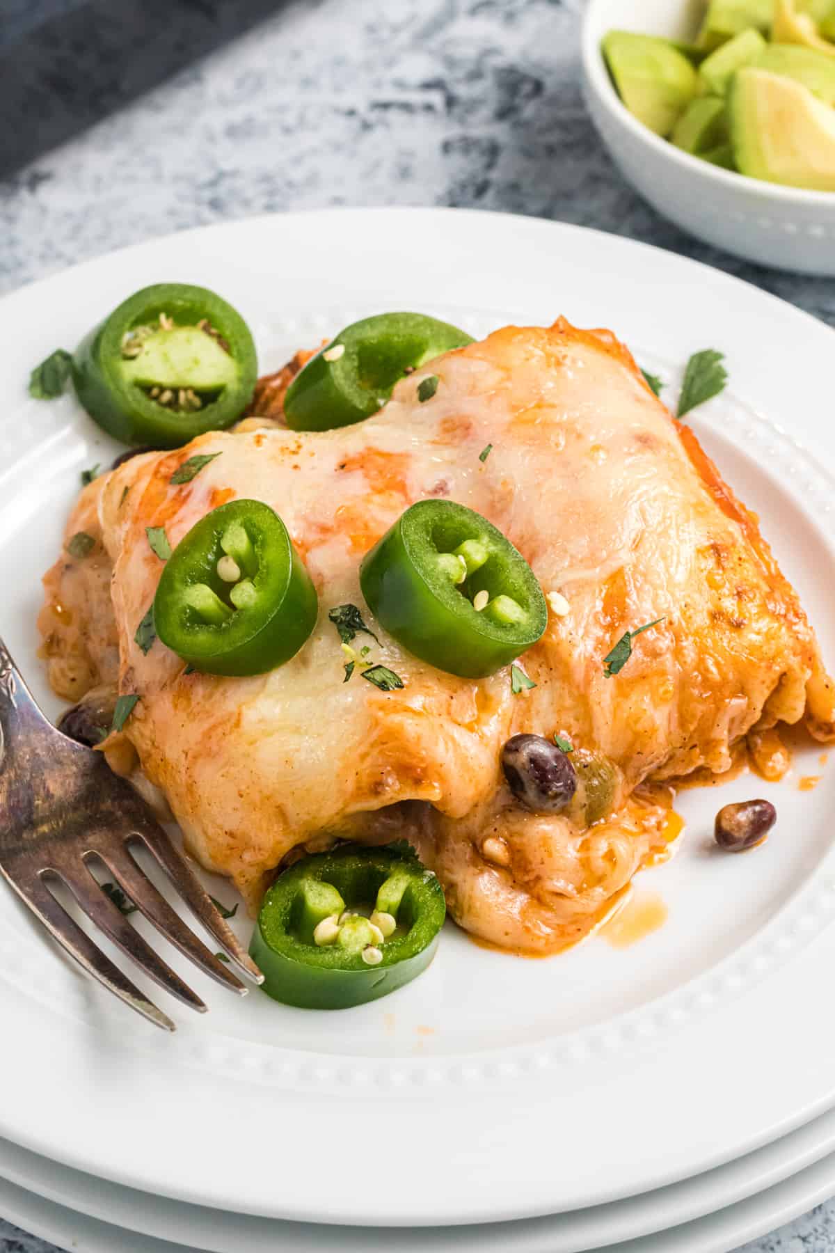 Several enchiladas are placed on a white plate and garnished with chopped jalapenos.