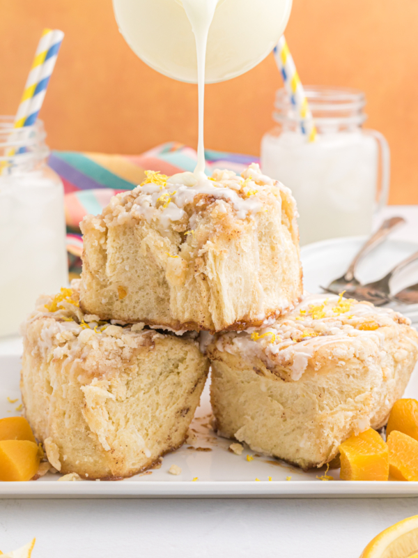 Three cinnamon rolls are being iced.