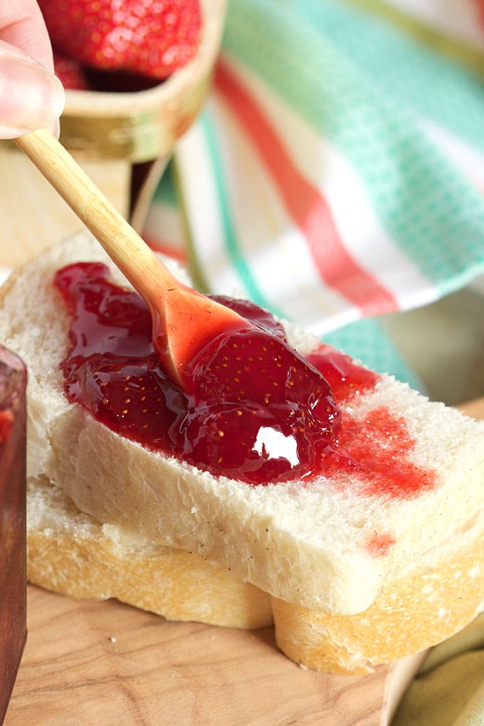 Strawberry jam being spread on a piece of white bread.