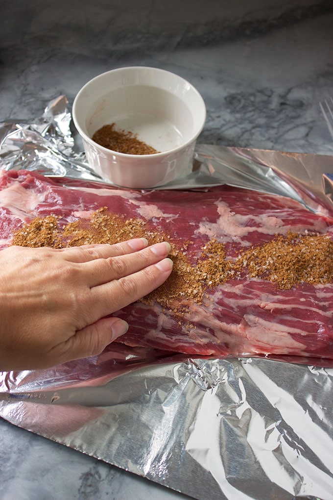 flank steak on foil with rub being applied.